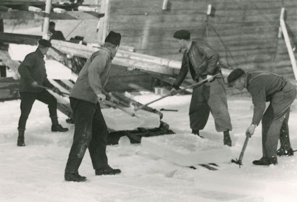 Fyra män hjälps åt med att få upp isblock för att få upp isen en kall vinterdag på 1940-talet.